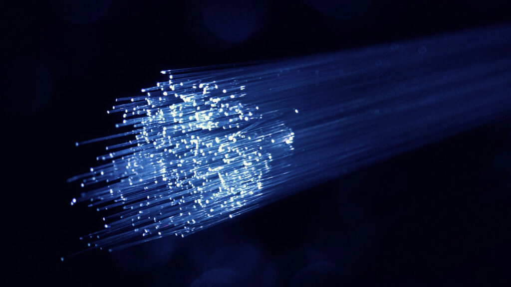 Dettaglio di un fascio di fibre ottiche con le terminazioni illuminate, blu su sfondo scuro.